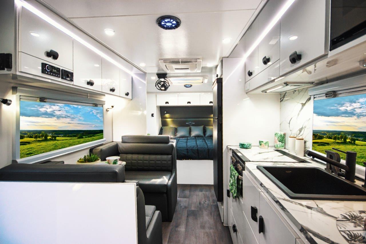 Interior of an Aussiemate caravan with cozy lounge seating, natural light, and integrated storage